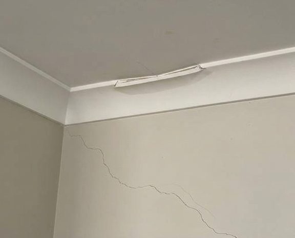 A cracked cornice run with the crack tracking down the wall below it, before the damaged length is cut out.
