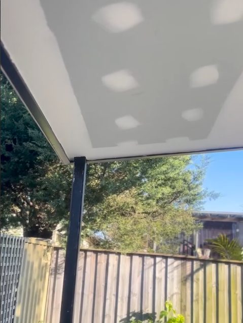 A patio ceiling lined and set, looking out through the posts to the trees and the fence line.