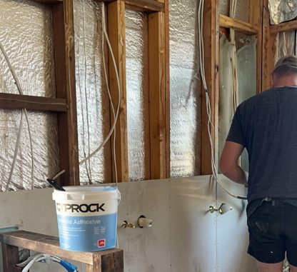 Wall lining going back on in a bathroom after a leak, with the framing and the insulation still exposed.